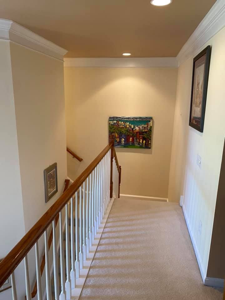 Stairwell with carpet and white railing, light beige walls, artwork, and crown molding.
