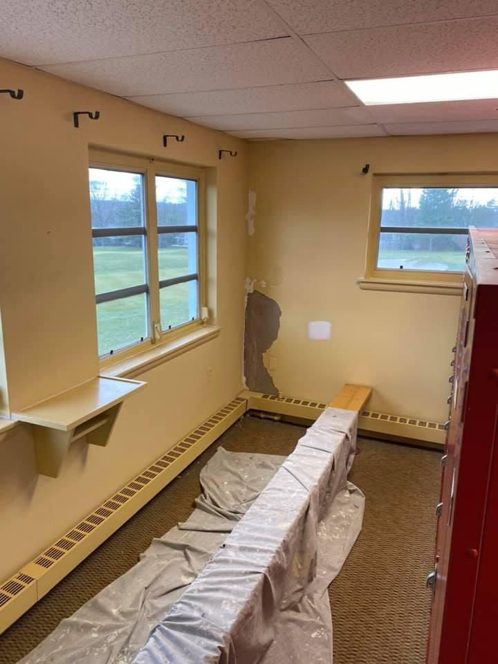 Interior of a room with yellow walls, two windows, a ceiling, and a long beam covered in plastic sheeting.