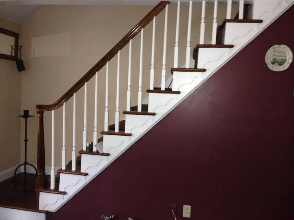 Staircase with wooden handrail and white balusters. Dark brown steps and maroon wall.