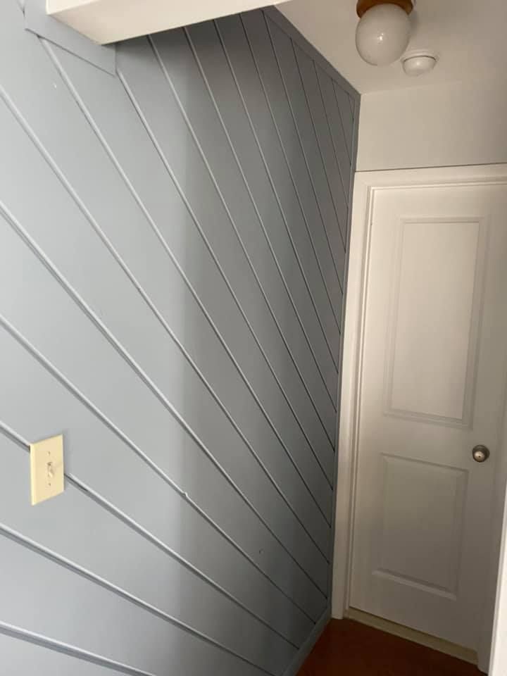 Light blue paneled wall next to a white door in a hallway. A light switch is visible on the wall.