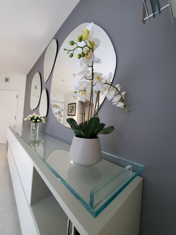 A vase of flowers sits on a glass shelf in front of a mirror