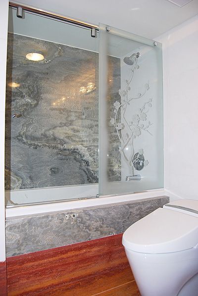 A bathroom with a toilet and a bathtub with a glass shower door.