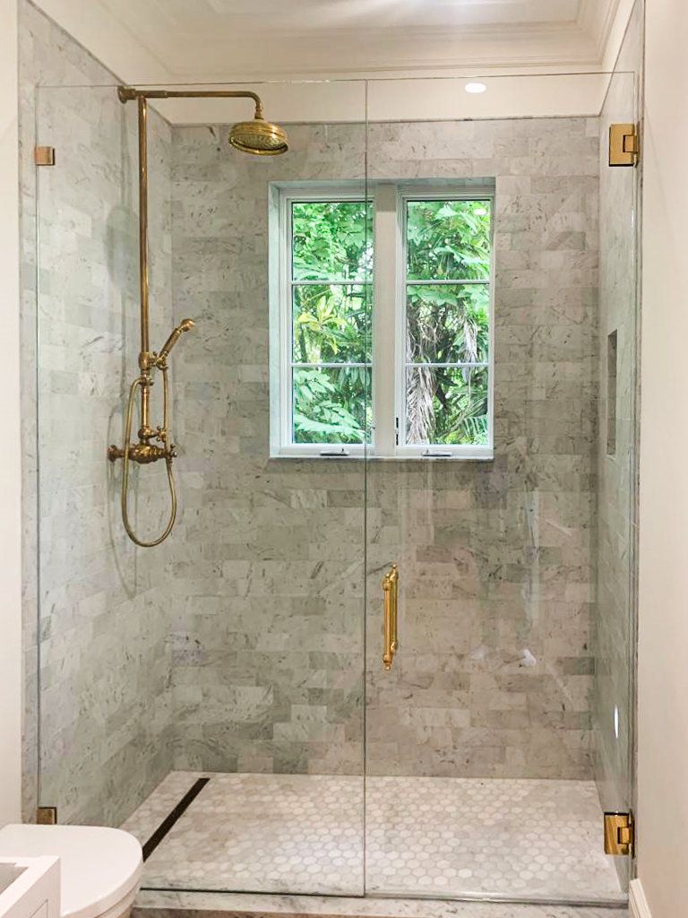 A bathroom with a walk in shower with a glass door and a window.