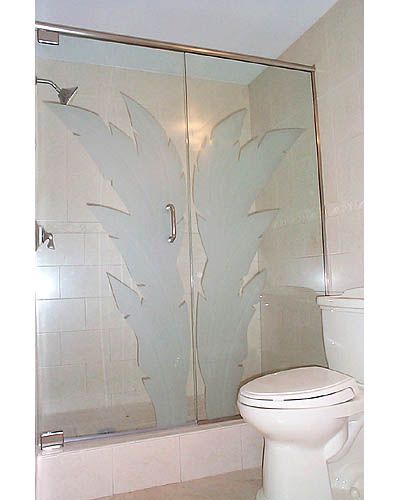 A bathroom with a toilet and a shower with a palm tree design on the door.