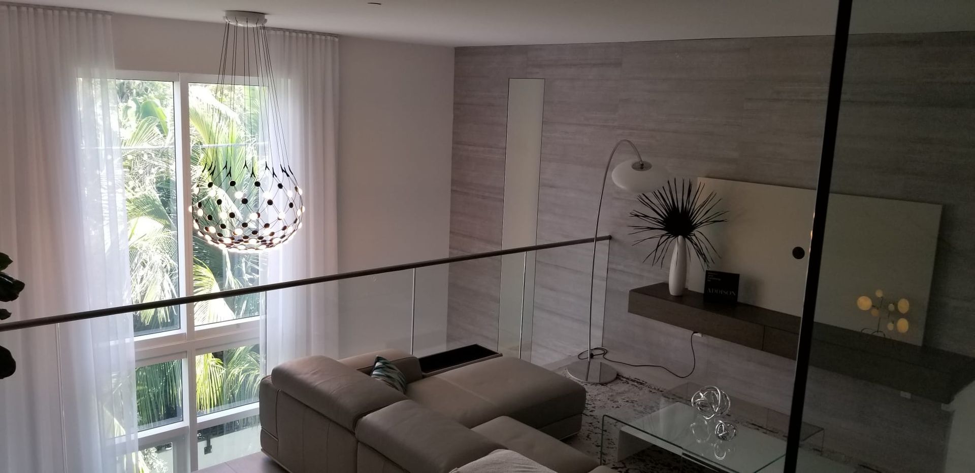 A living room with a couch, ottoman, and a glass railing.