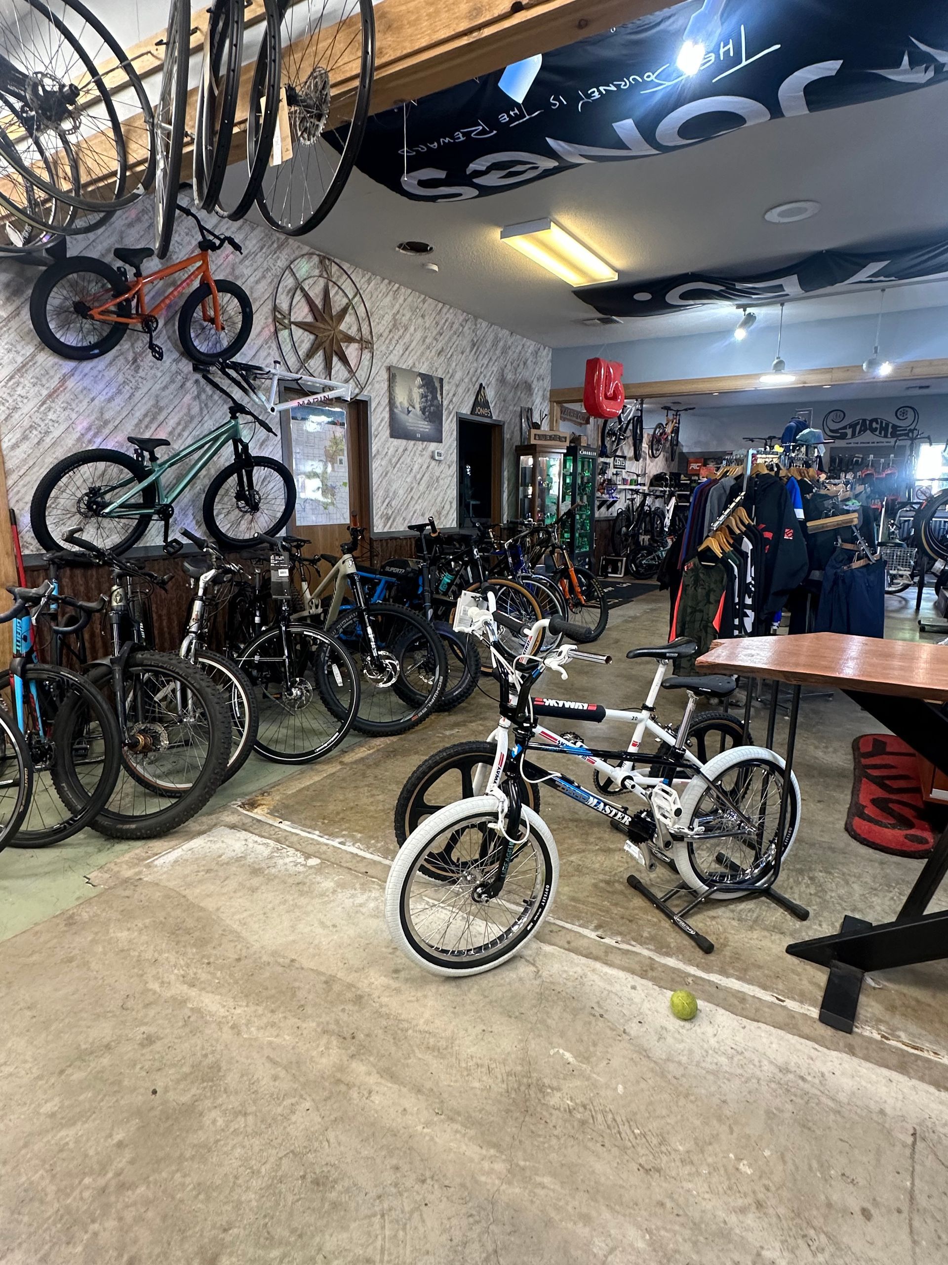 Bicycle shop interior with many bikes displayed on walls and floor, and a small white bike in front.