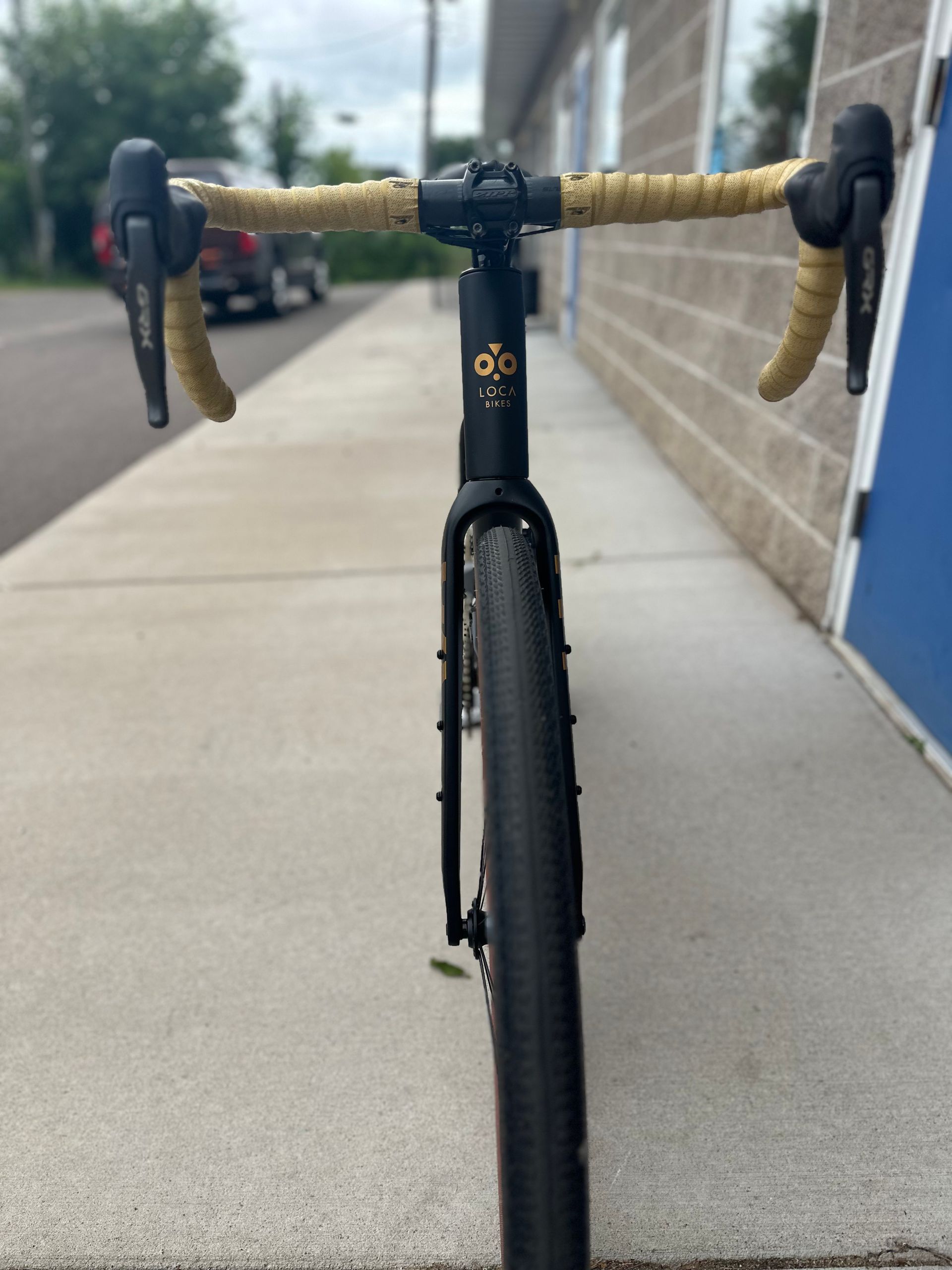 Front view of a black road bike with tan handlebars on a wet sidewalk by a brick wall