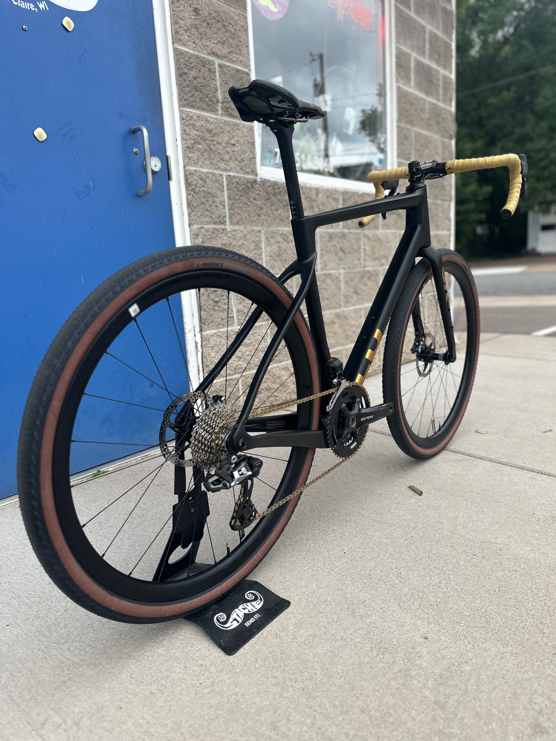 Black road bike with tan tires leaned against a blue wall indoors