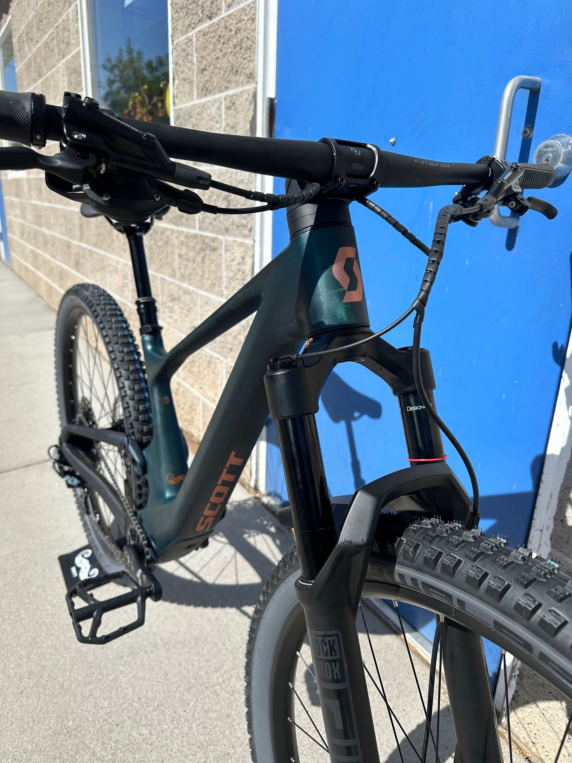 Black mountain bike parked beside a blue wall in sunlight