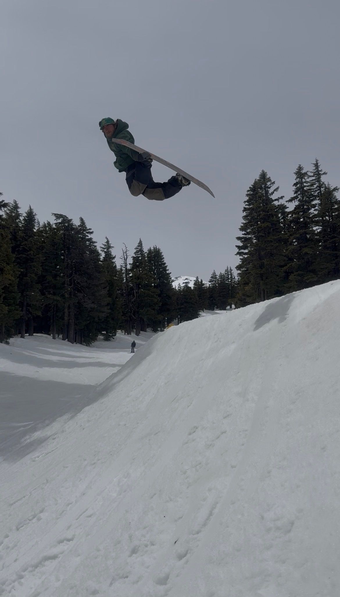 Snowboarder performing an aerial trick above a snowy halfpipe under a gray sky