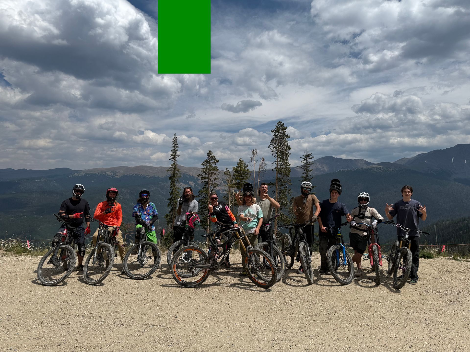 Cyclists lined up on a gravel overlook with mountains and cloudy sky in the background