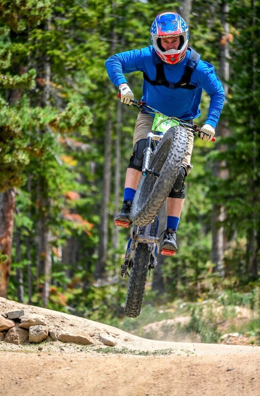 Mountain biker in blue gear airborne over a dirt trail in a forest