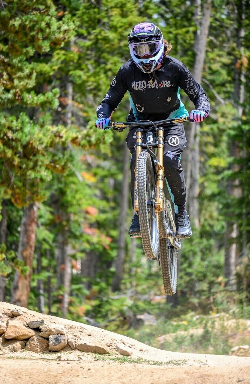 Mountain biker airborne on a forest trail, wearing a helmet and black gear.