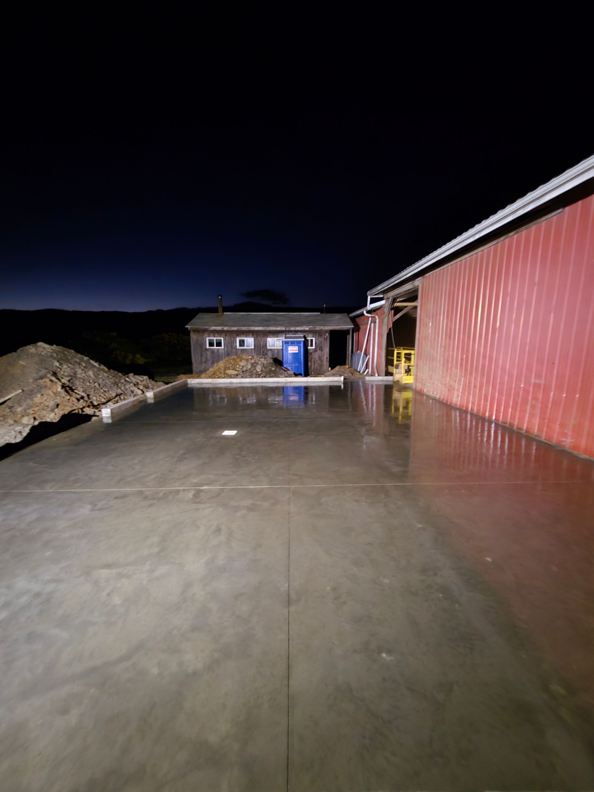 A concrete driveway with a red barn in the background at night.