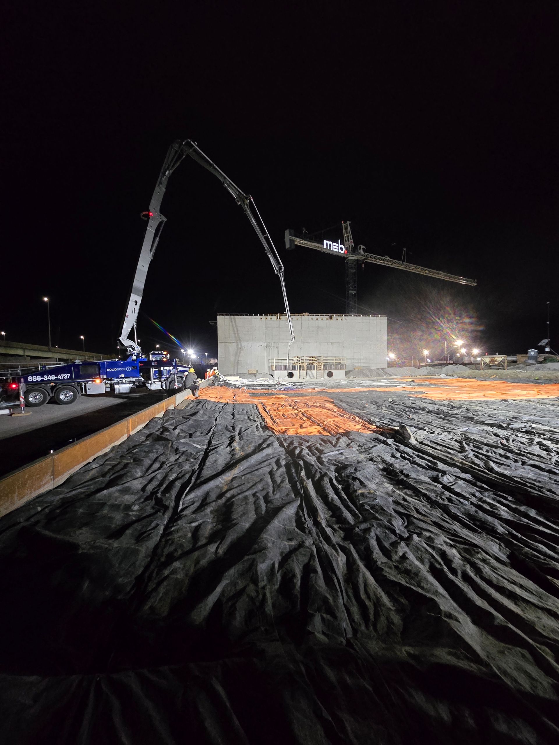 A construction site at night with a crane pumping concrete.