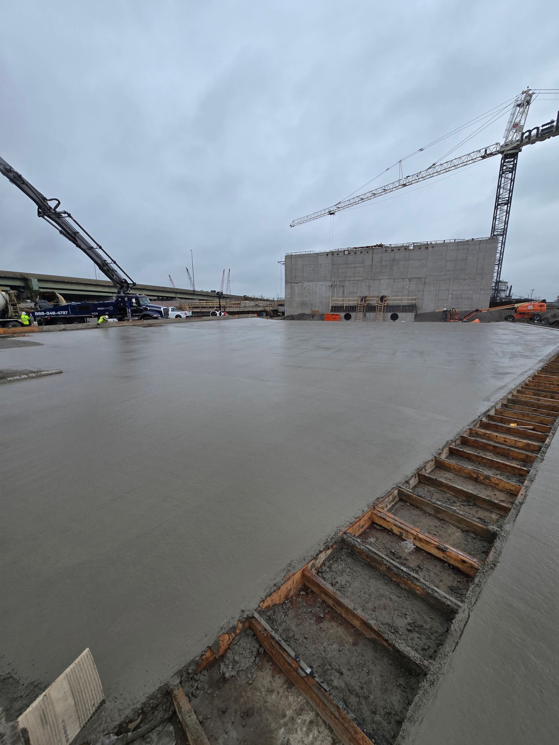 A concrete floor is being poured in a construction site with a crane in the background.