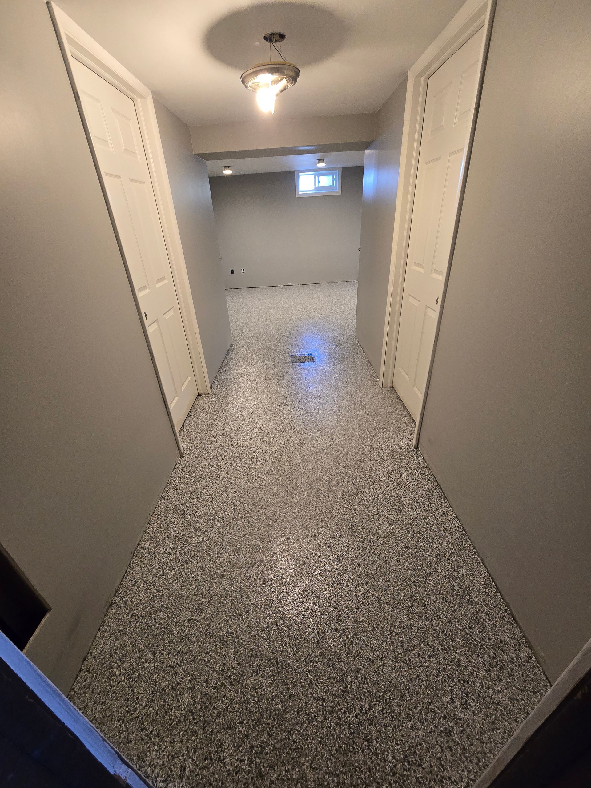 A hallway in a house with a gray floor and white doors.