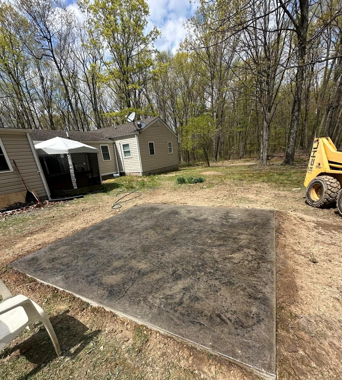 A yellow tractor is driving down a dirt road in front of a house.