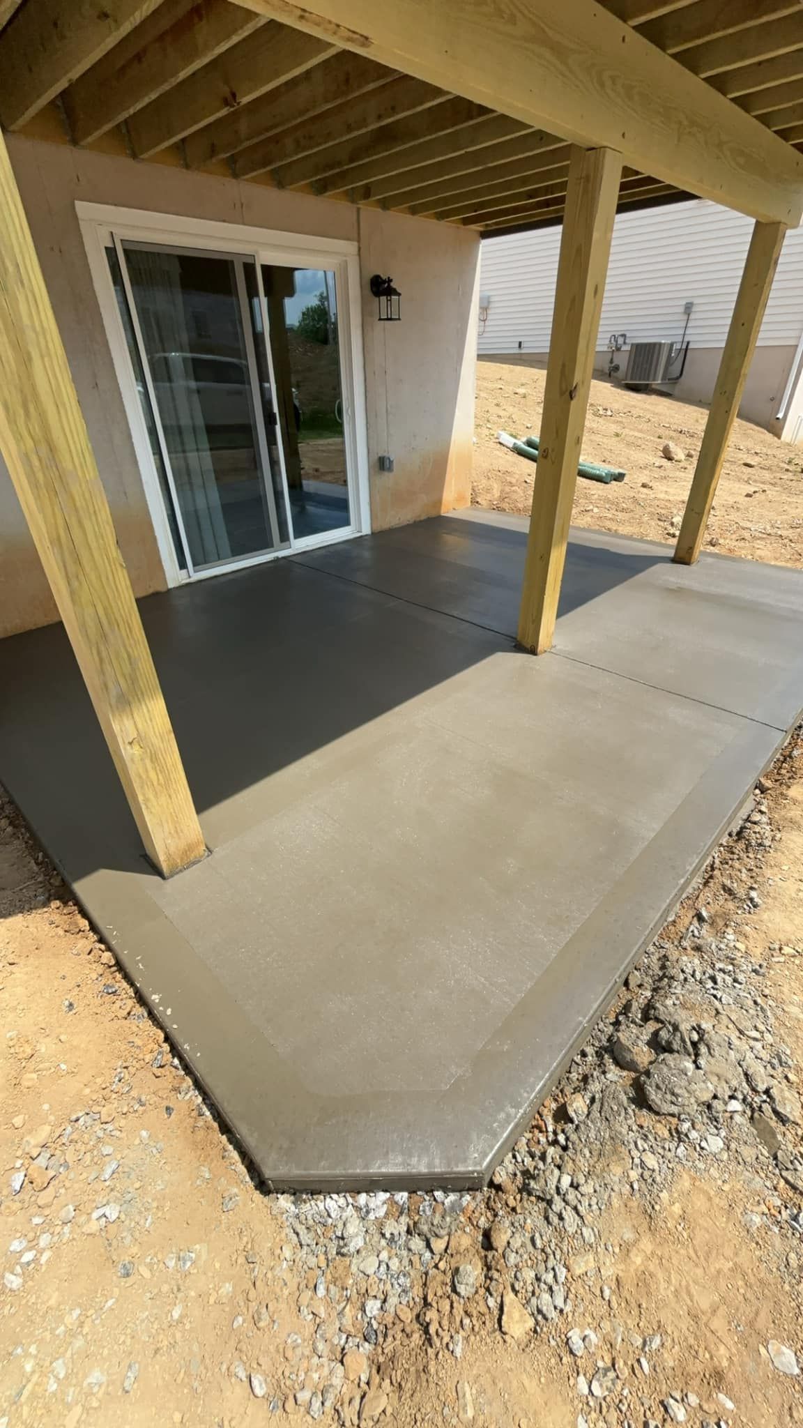 A concrete patio under a wooden deck with a sliding glass door.