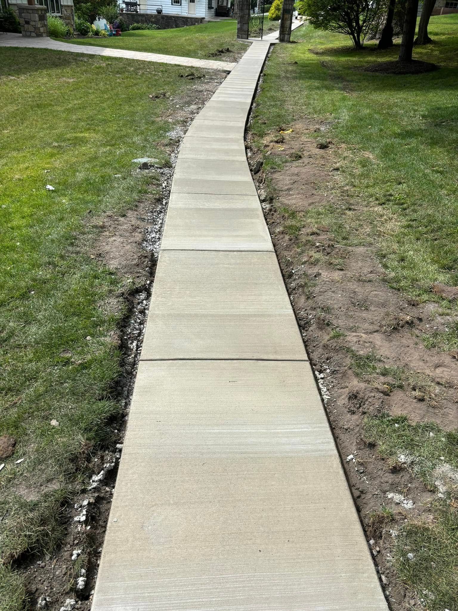 A long concrete walkway going through a grassy field.