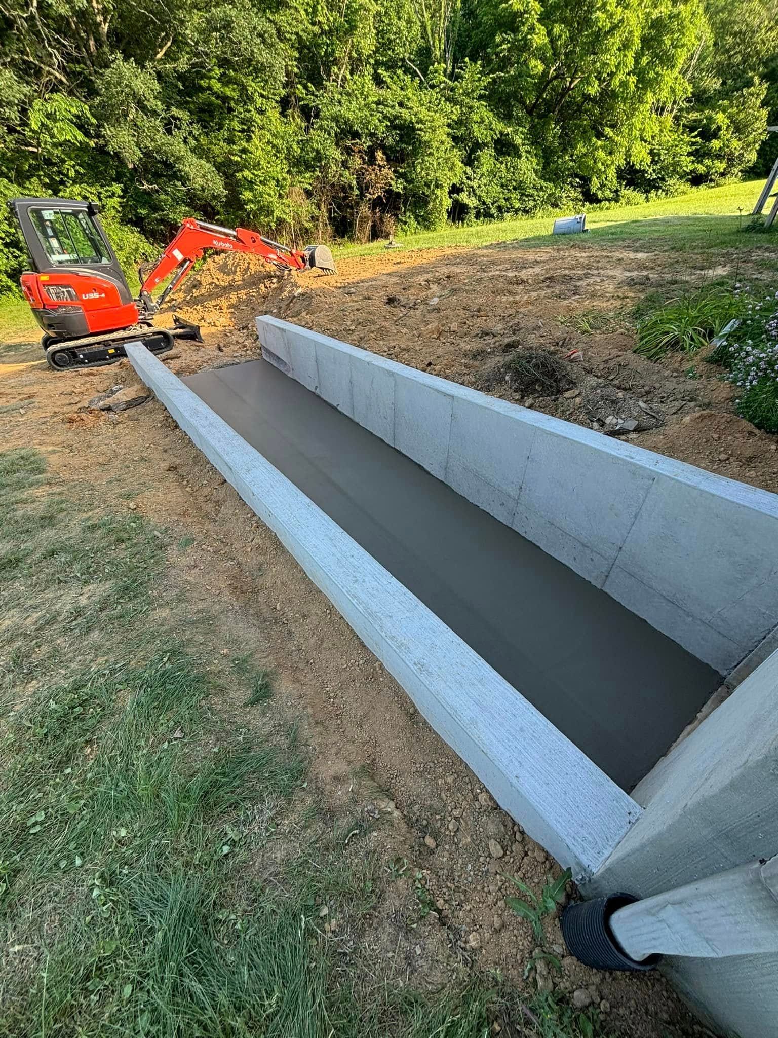 A small excavator is working on a concrete ramp.