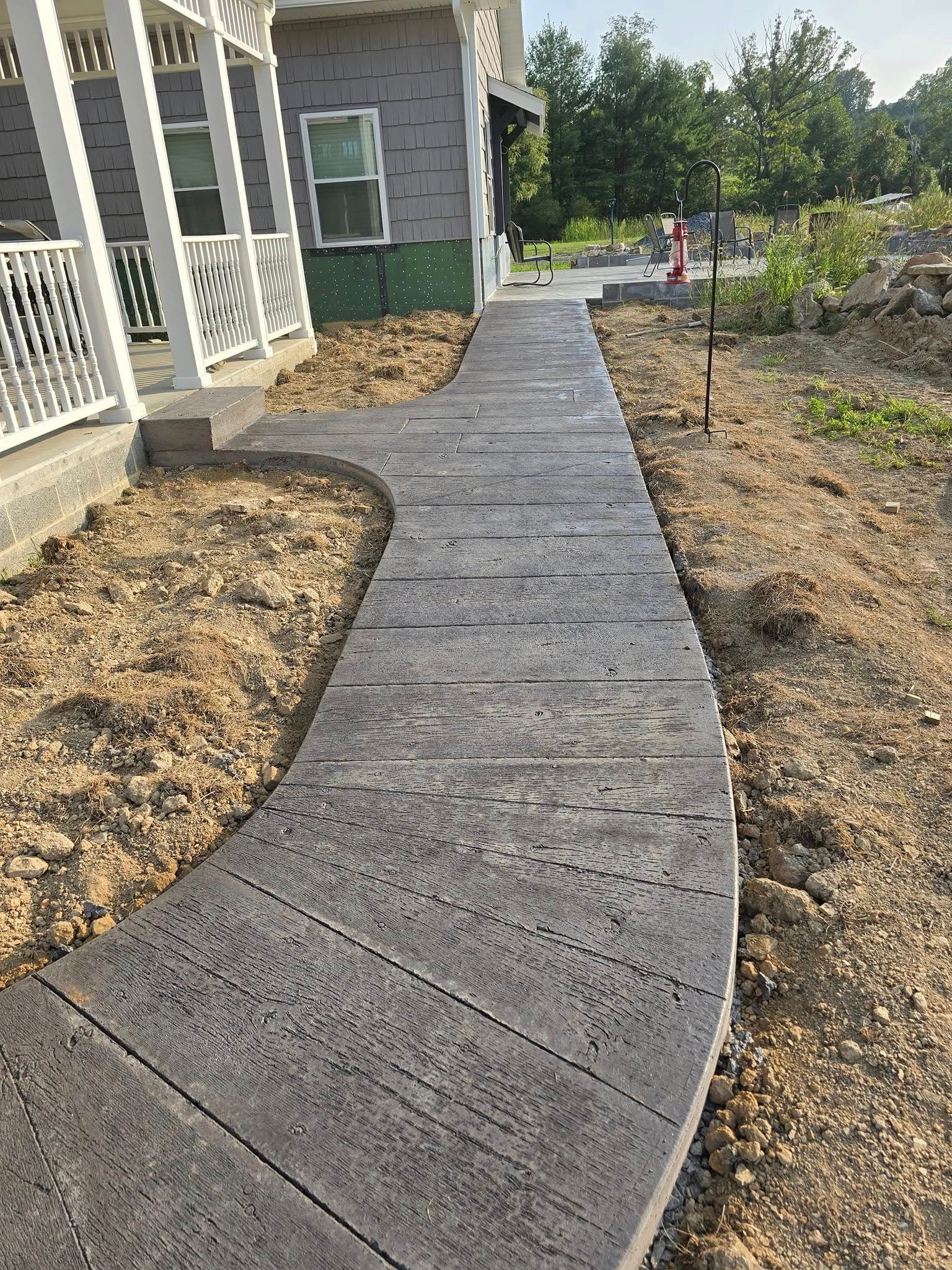A concrete walkway leading to a house with a porch.