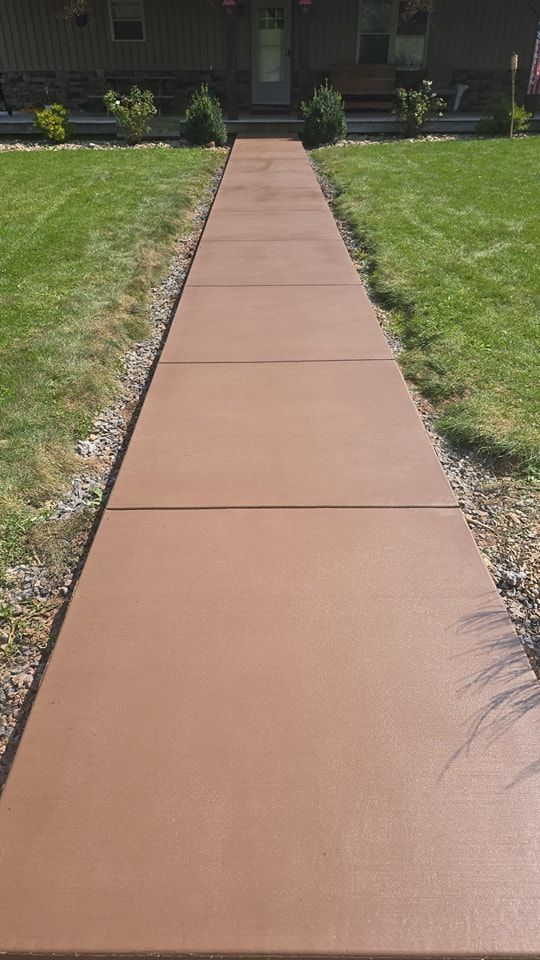 A concrete walkway leading to a house with a lush green lawn.