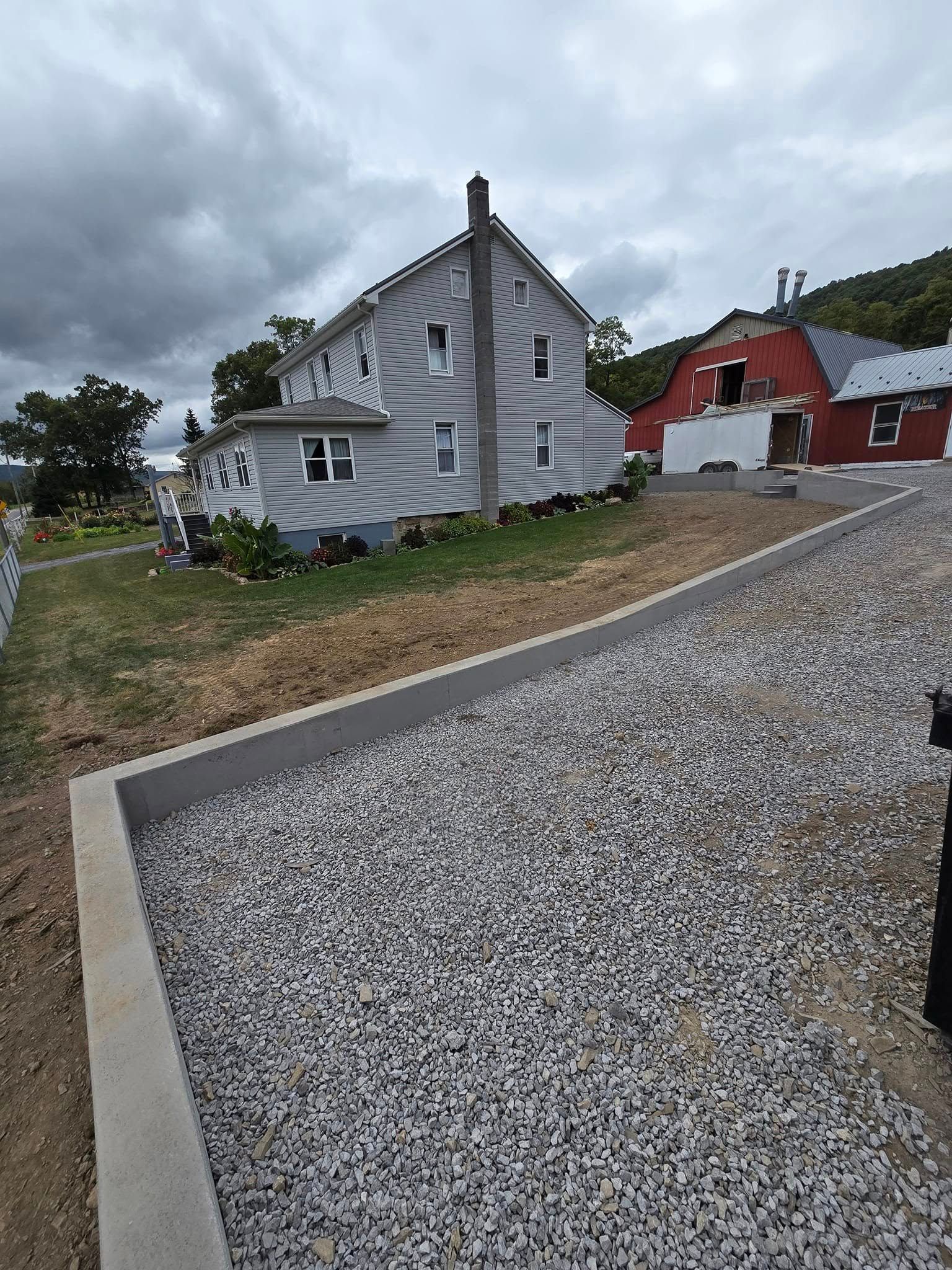 A white house with a red barn in the background is sitting next to a gravel driveway.