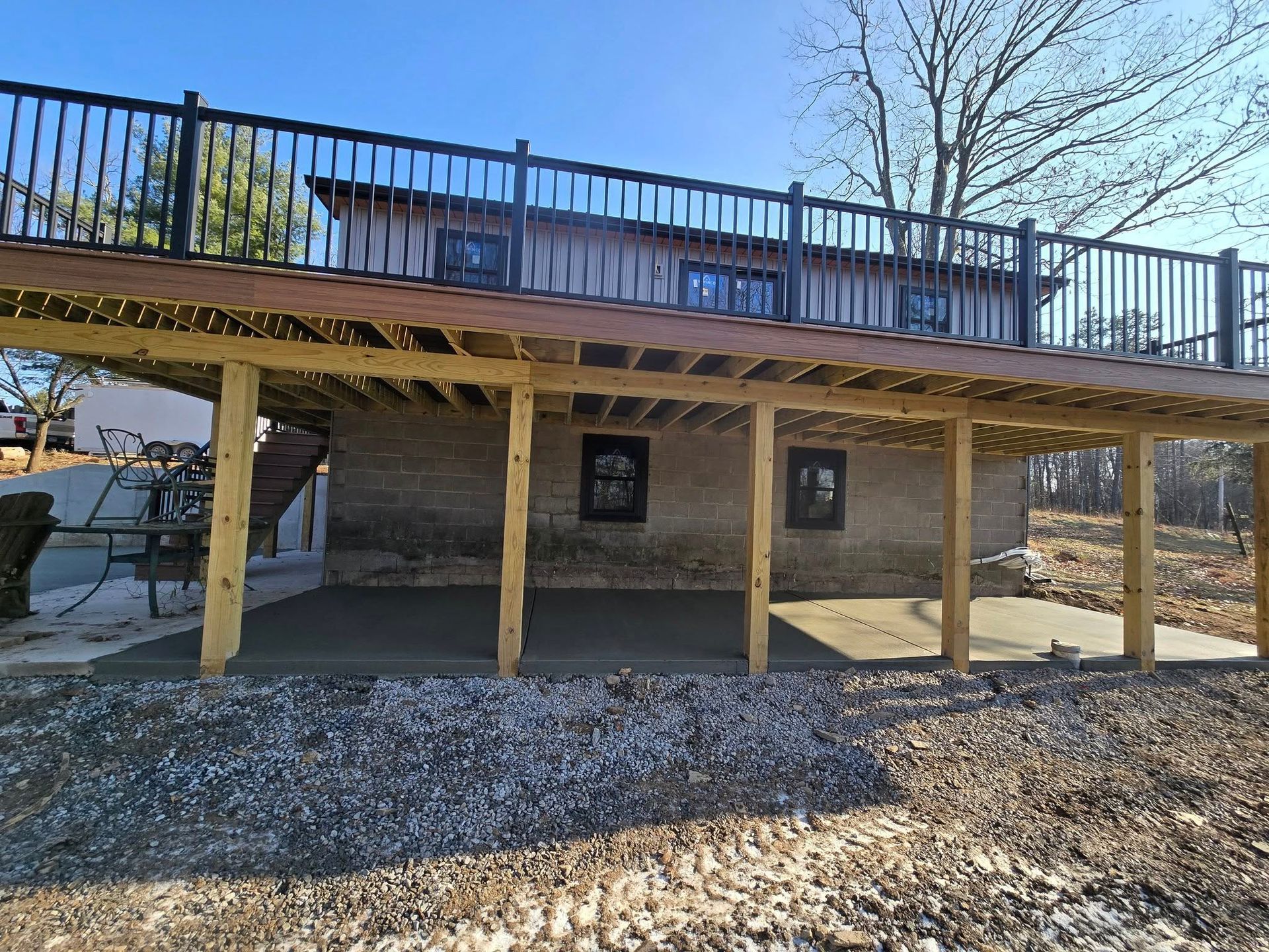 A wooden deck with a black railing is sitting under a house.