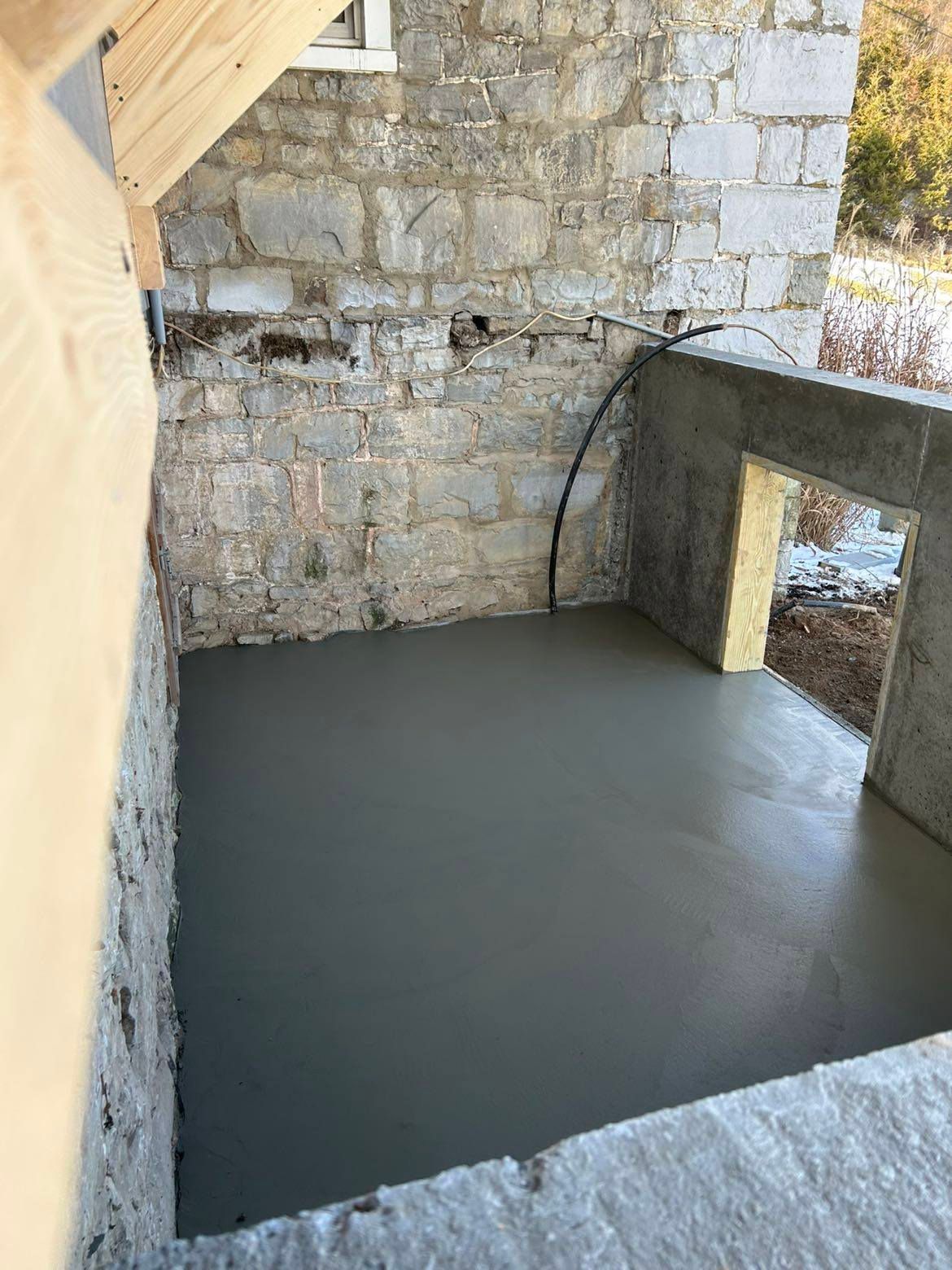 A concrete floor is being poured in a room next to a stone wall.