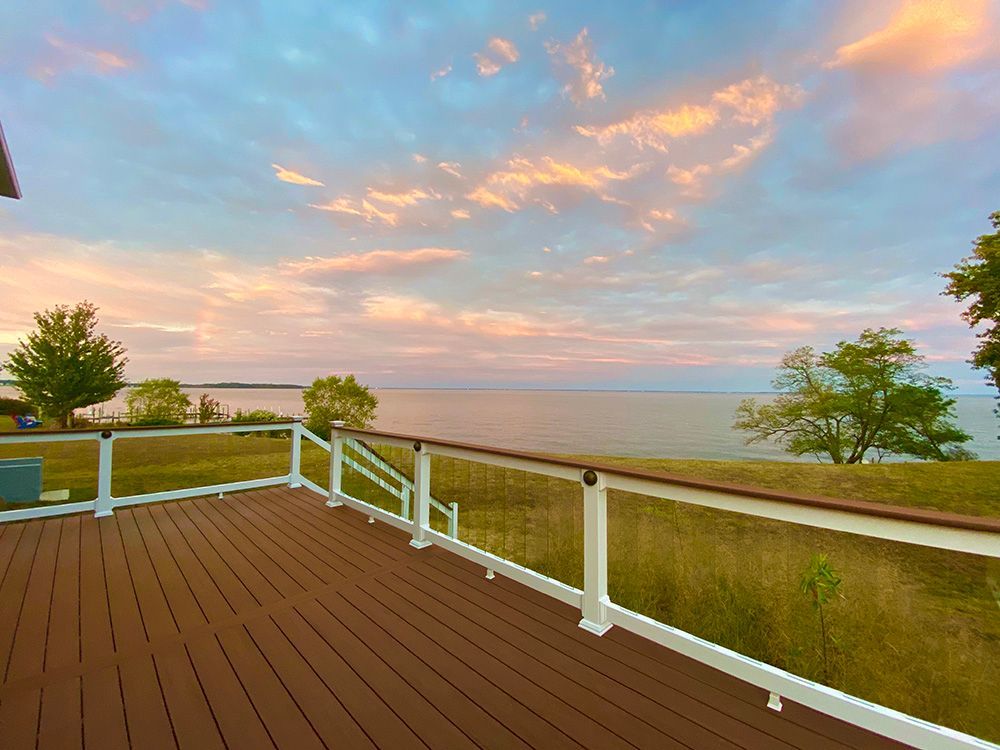 Wooden deck overlooking calm water at sunset with pink clouds and white railings