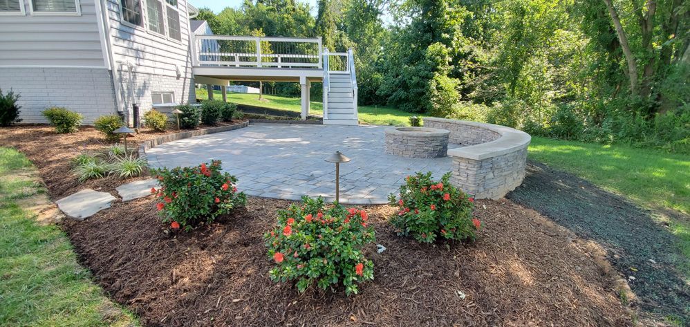 Backyard patio with stone fire pit, flower beds, and a white deck beside a house