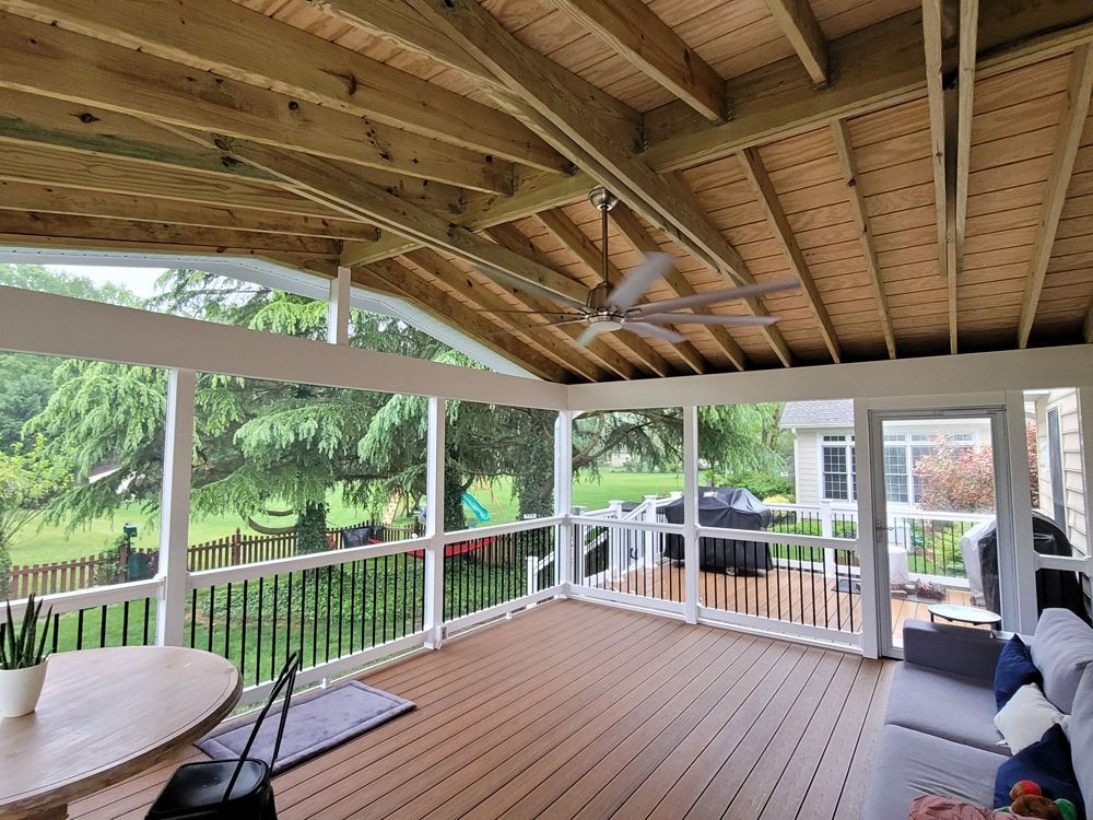 Covered wooden porch with a ceiling fan, railing, and outdoor seating overlooking a green yard