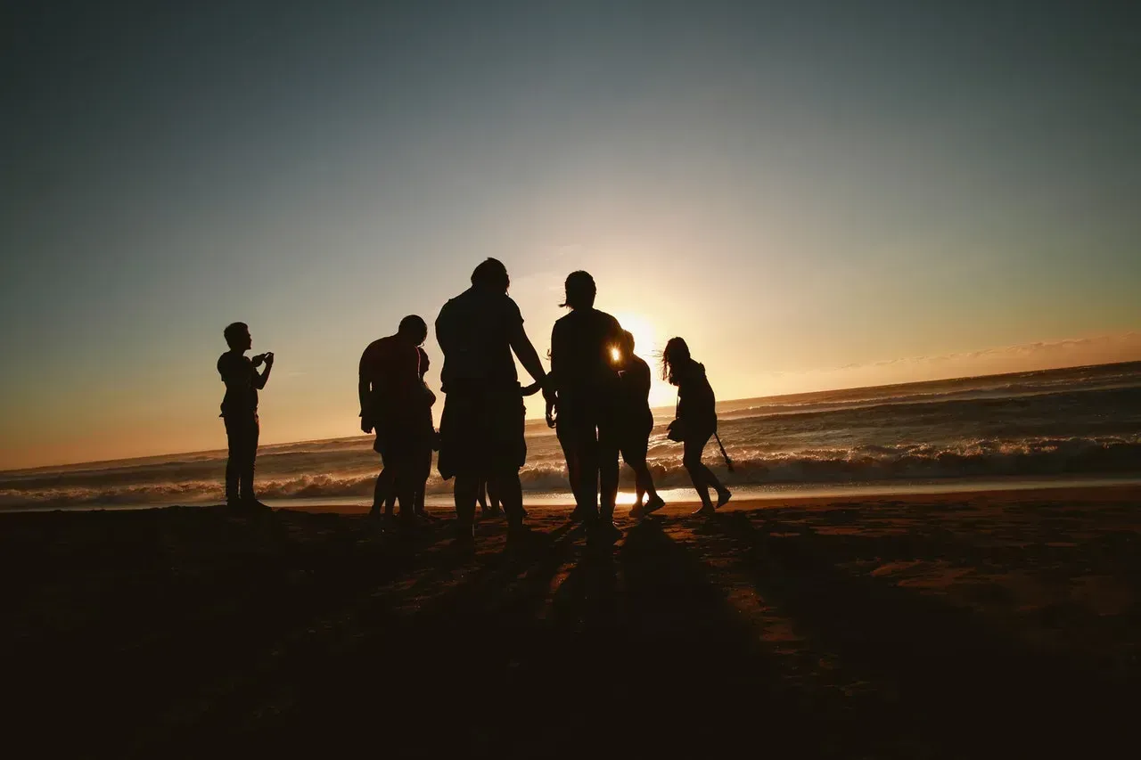 Silhouetted people standing and walking on a beach at sunset, with the ocean in the background