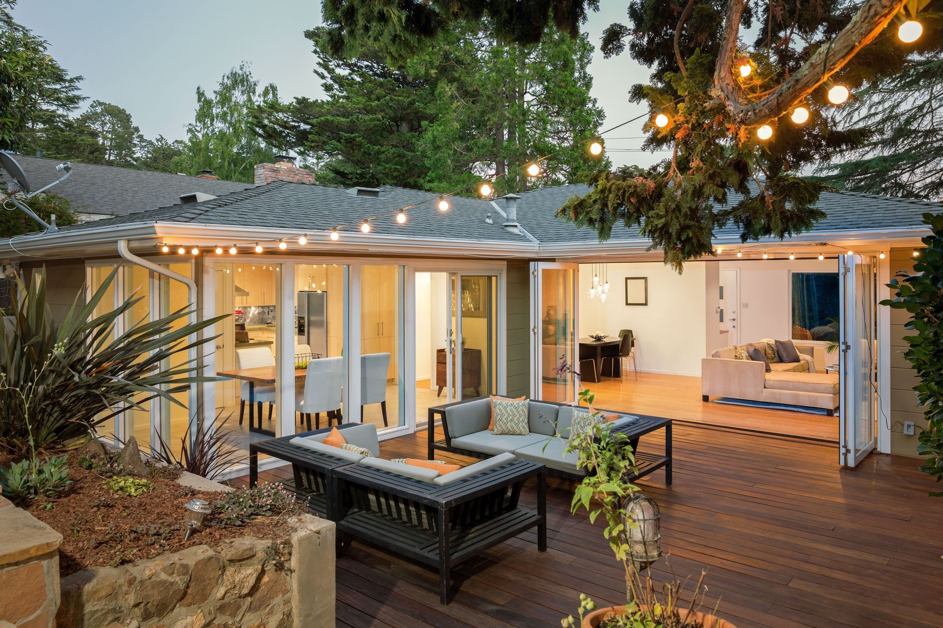 Cozy outdoor patio with string lights, wicker seating, and a modern house interior visible through open doors