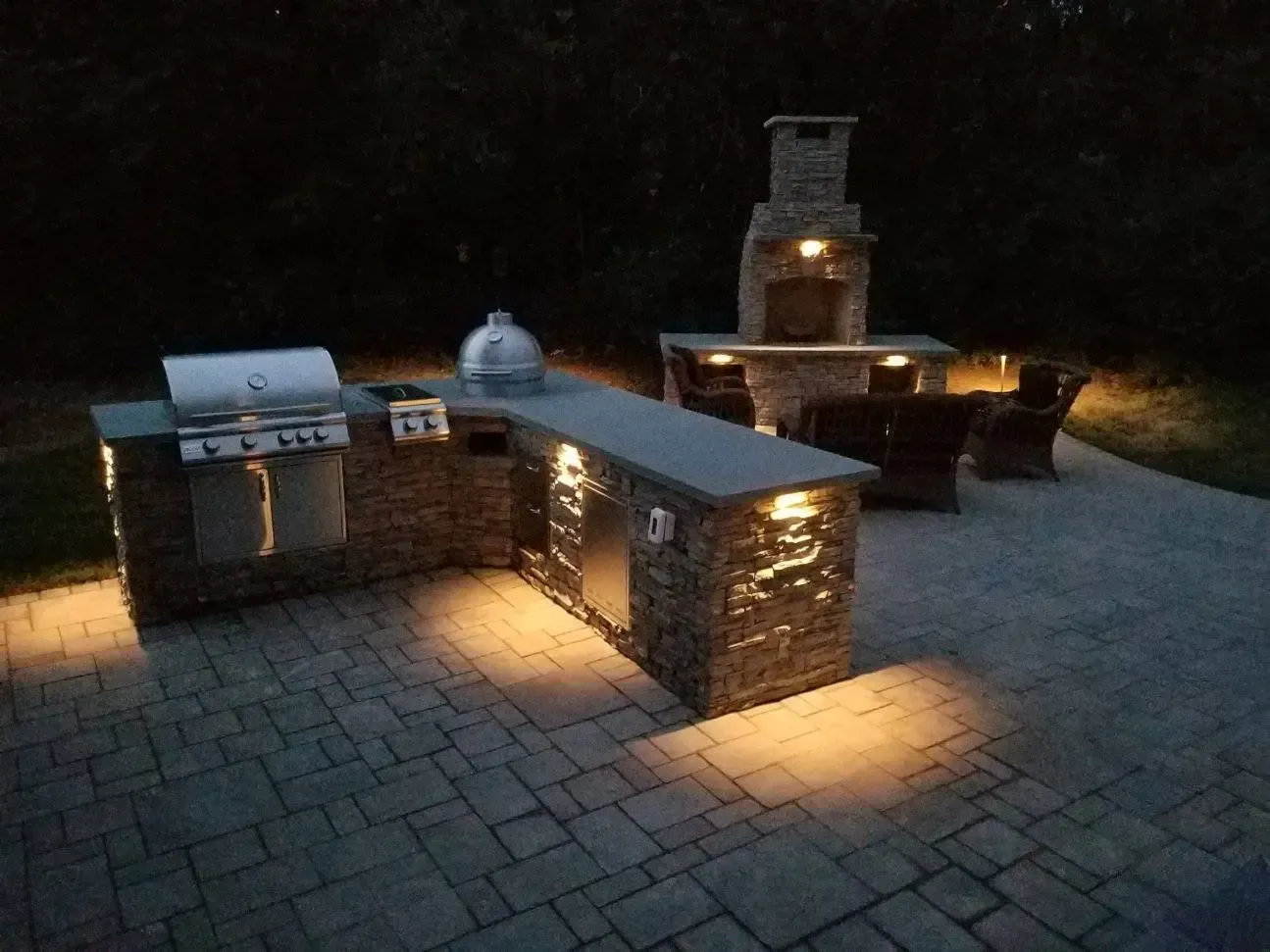 Outdoor stone patio with built-in grill, countertop, and fire pit lit at night
