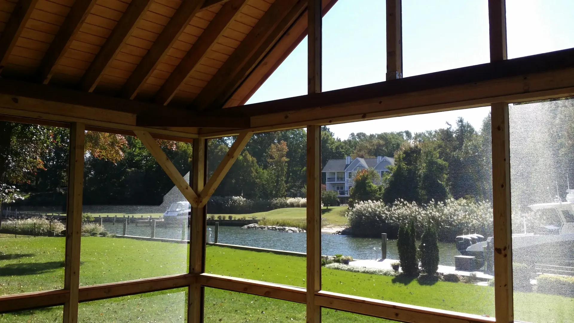 Wooden gazebo overlooking a green lawn and pond on a sunny day