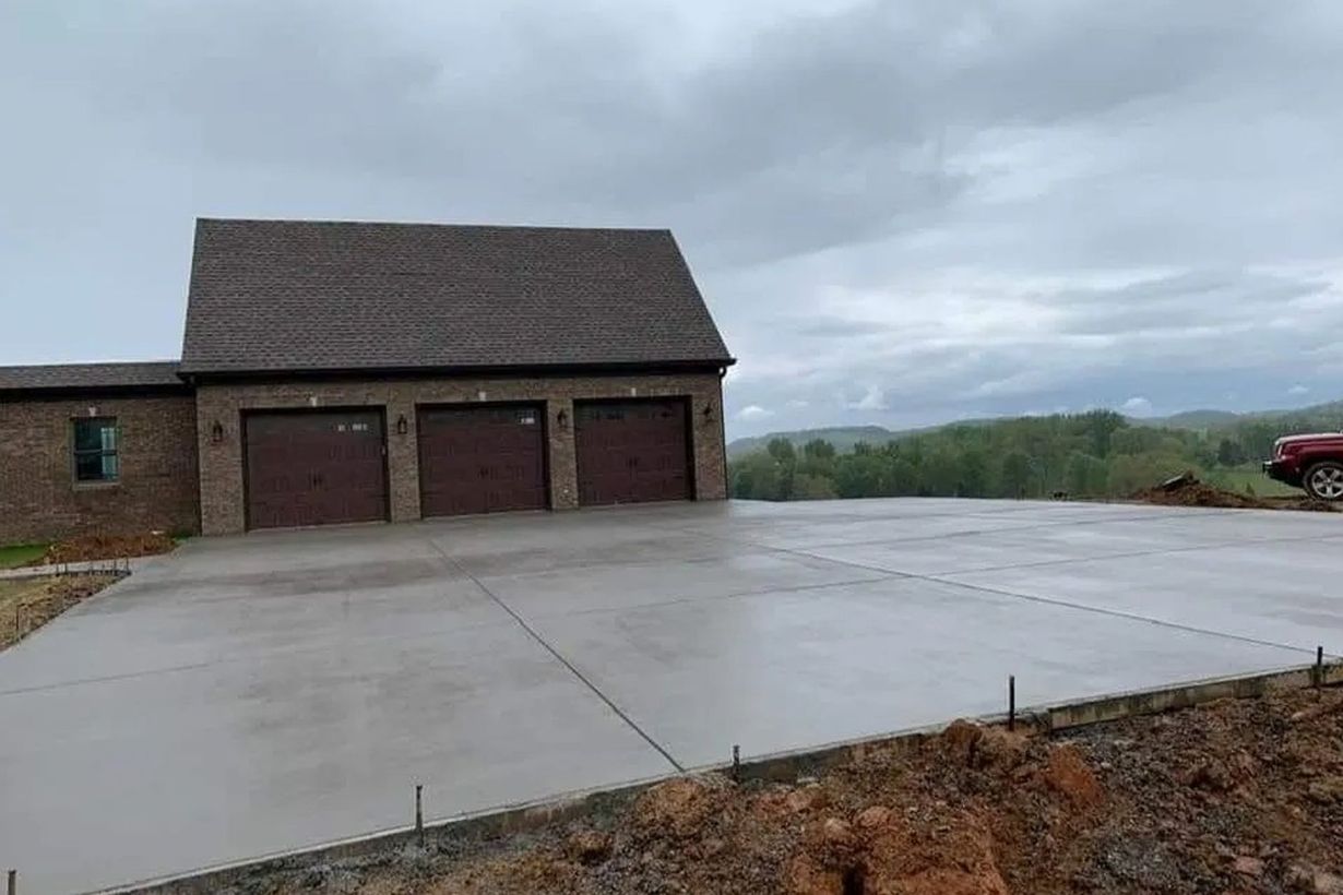 Newly poured concrete driveway in front of a brick garage under an overcast sky.