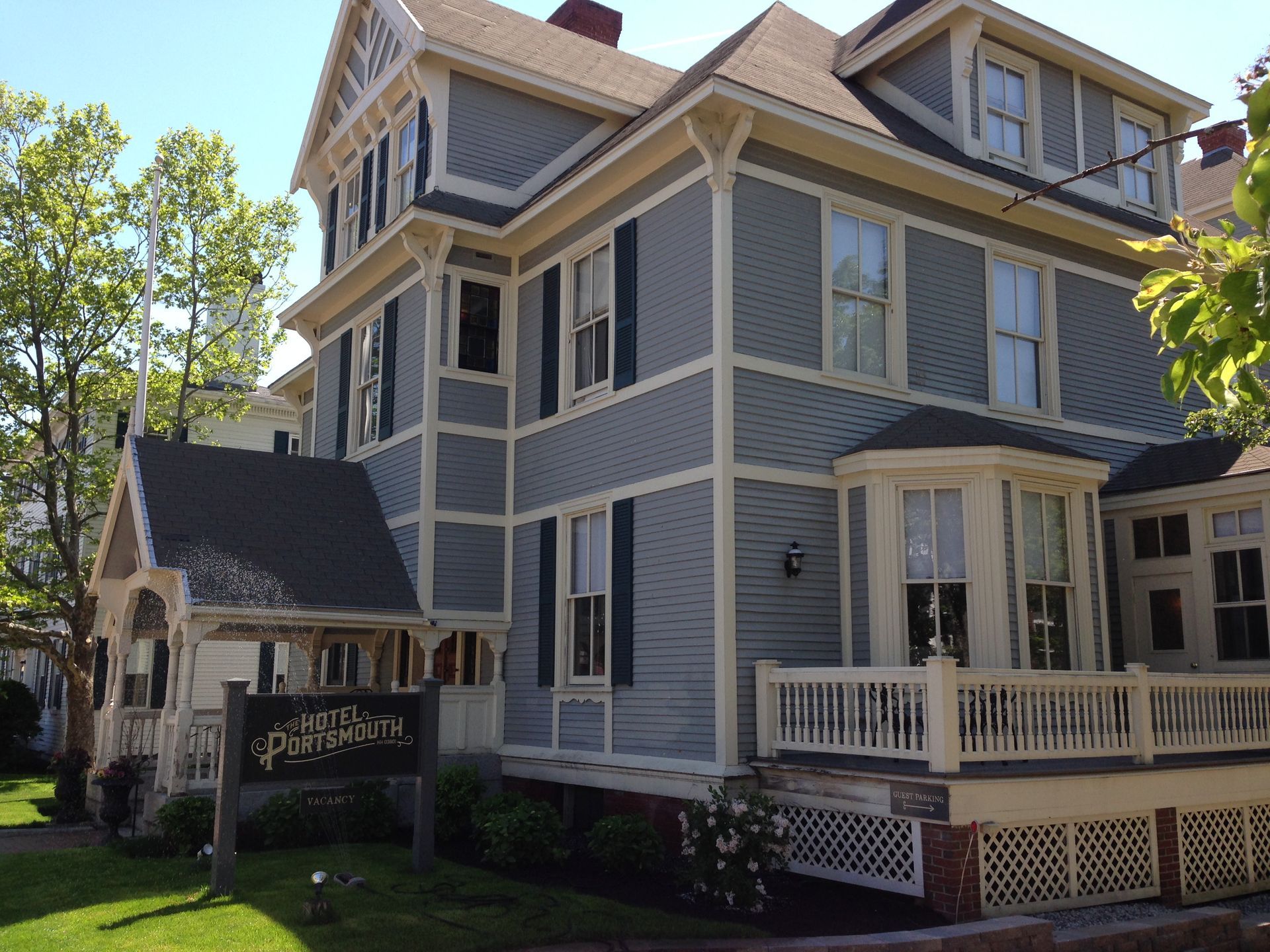 Gray Victorian-style house with white trim, porch, and a sign in front on a sunny day