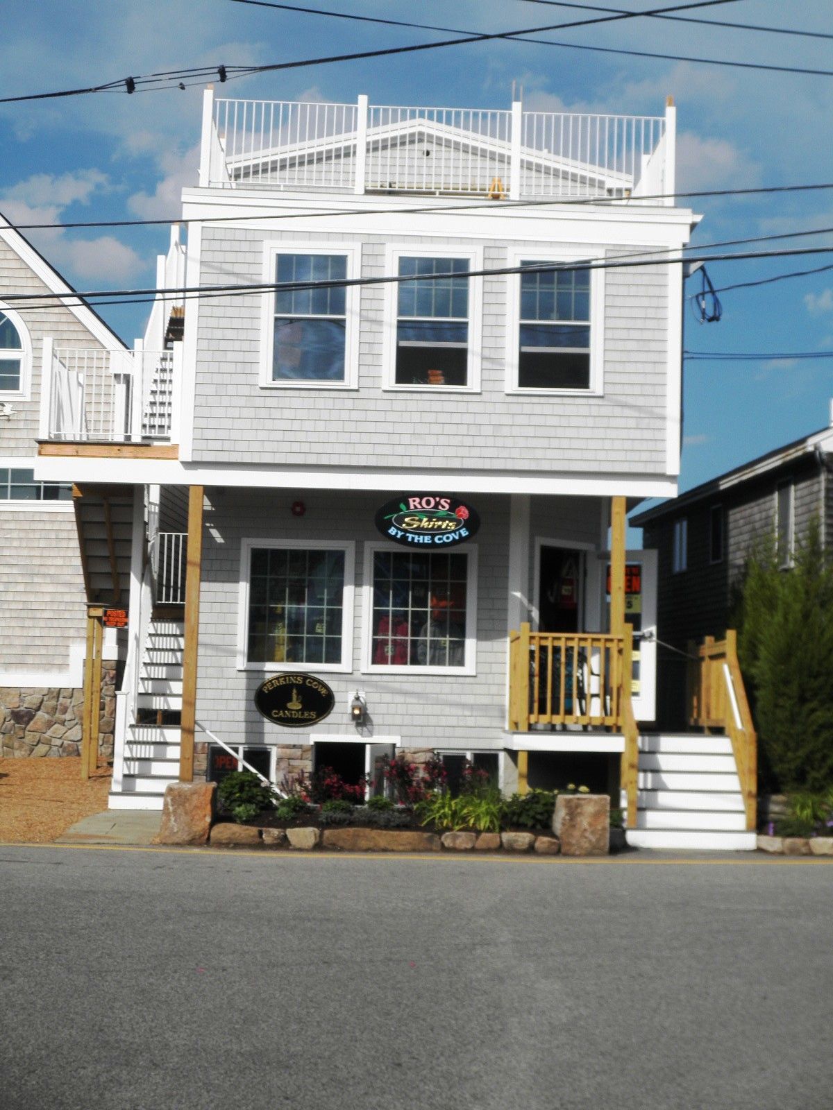 White two-story storefront with front porch, rooftop deck, and yellow stairs under a blue sky