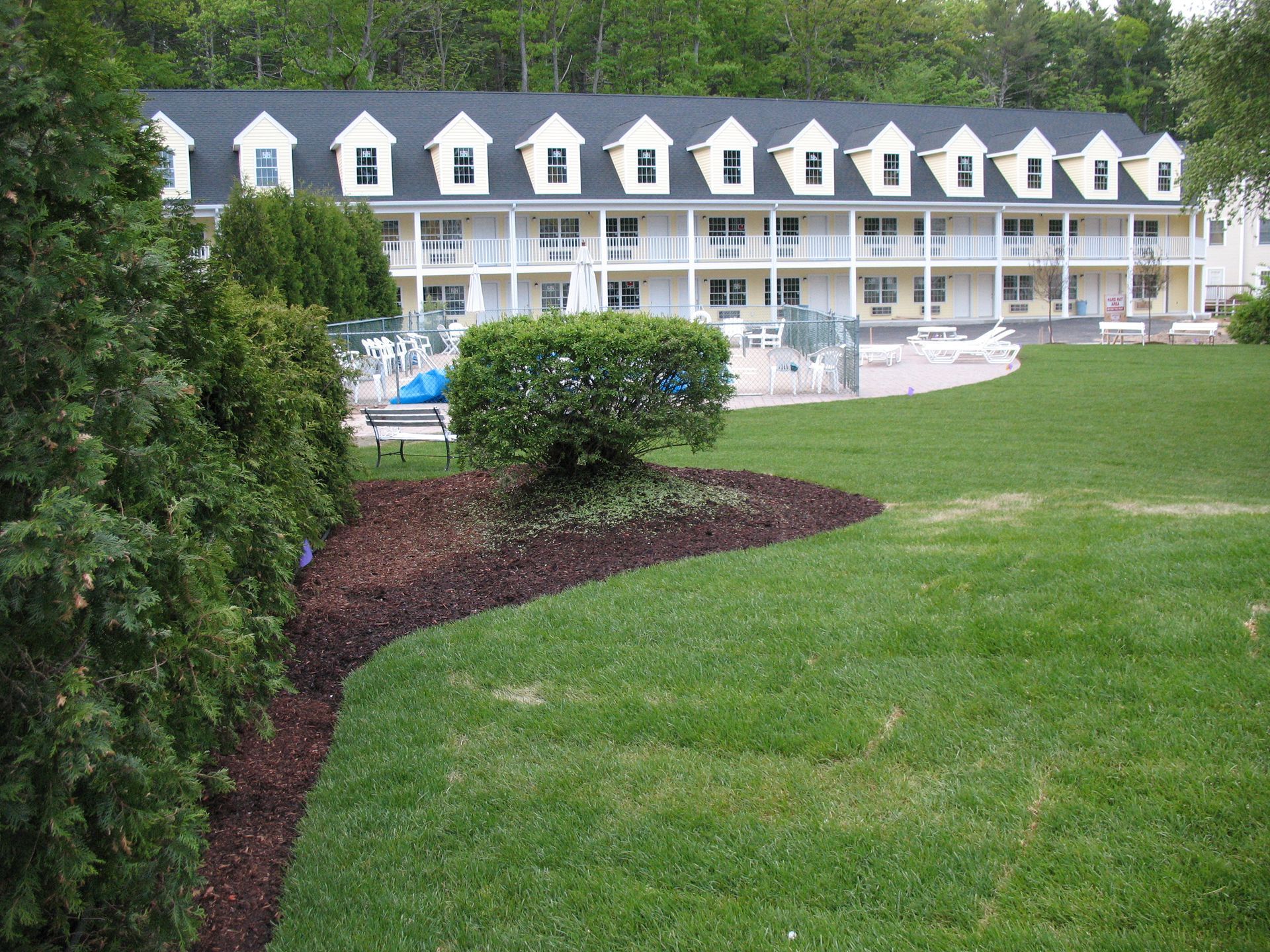 Grassy courtyard with a white motel-style building, rows of dormer windows, and a small pool