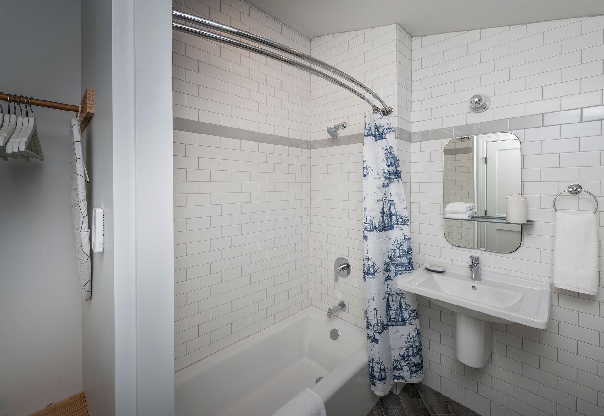 Small white-tiled bathroom with a tub, sink, mirror, and blue patterned shower curtain.