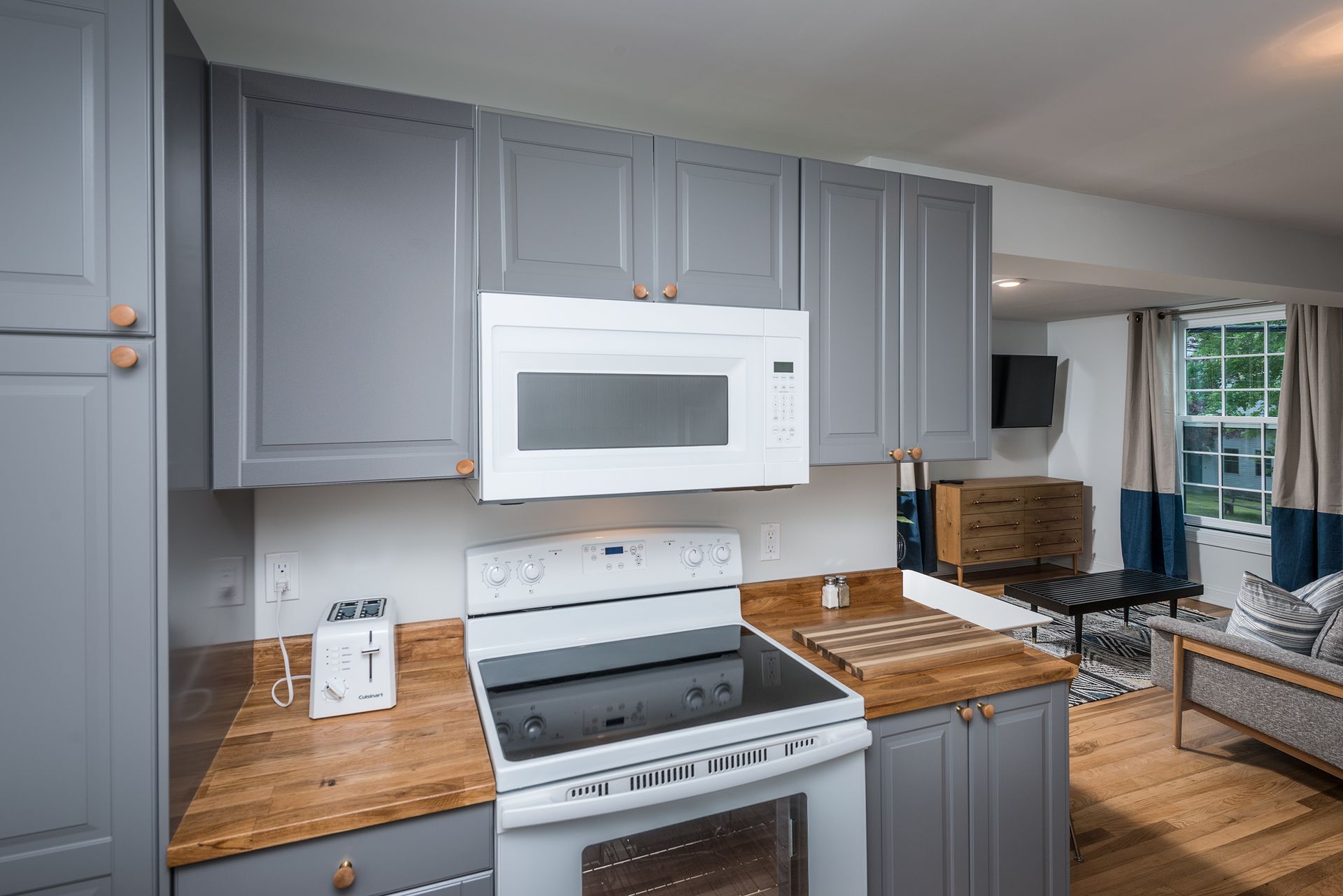 Gray kitchen with white appliances, wood counters, and a view into a living room and windowed dining area