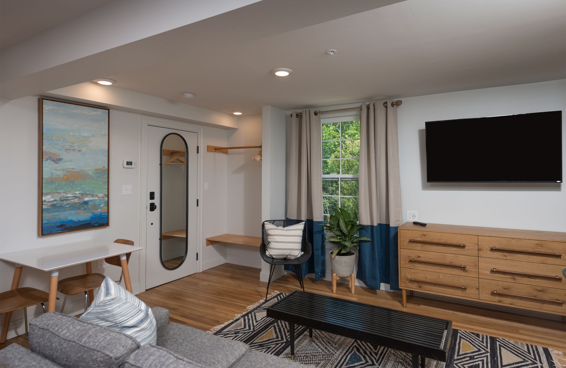 Modern living room with gray sofa, wall-mounted TV, wooden dresser, and large window curtains