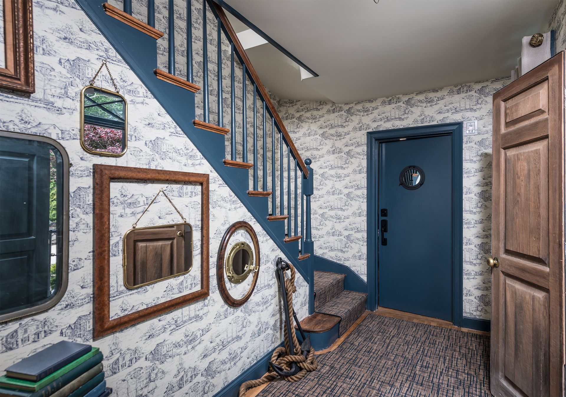 Stairway in a rustic home entryway with blue trim, framed wall decor, and a blue front door