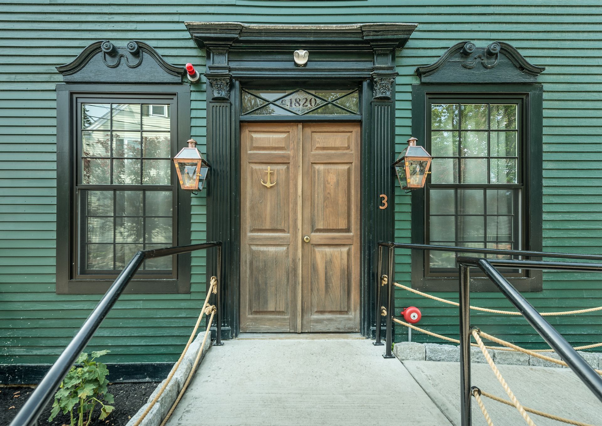 Front entrance of a teal building with double wooden doors, windows, lanterns, and wheelchair ramps.