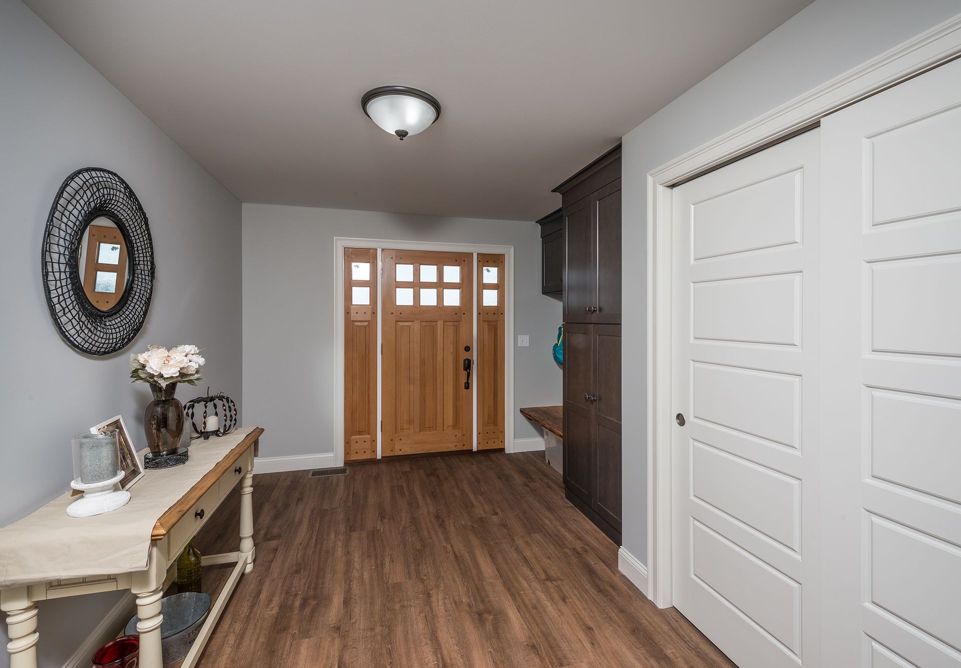 Hallway with wood floors, front door, white closet doors, and a console table with decor and flowers.