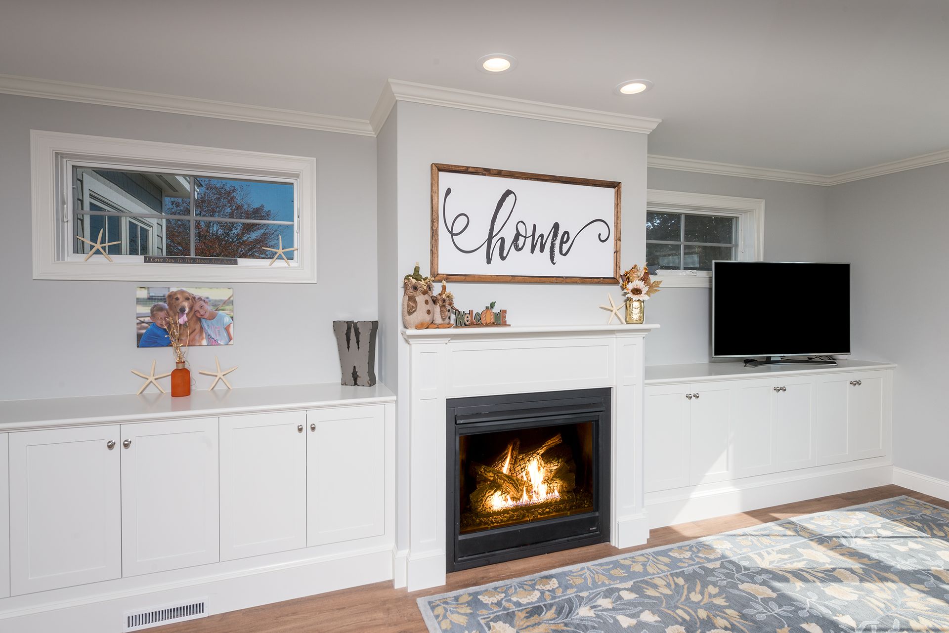 Bright living room with white built-ins, fireplace, wall art, TV, and patterned blue rug