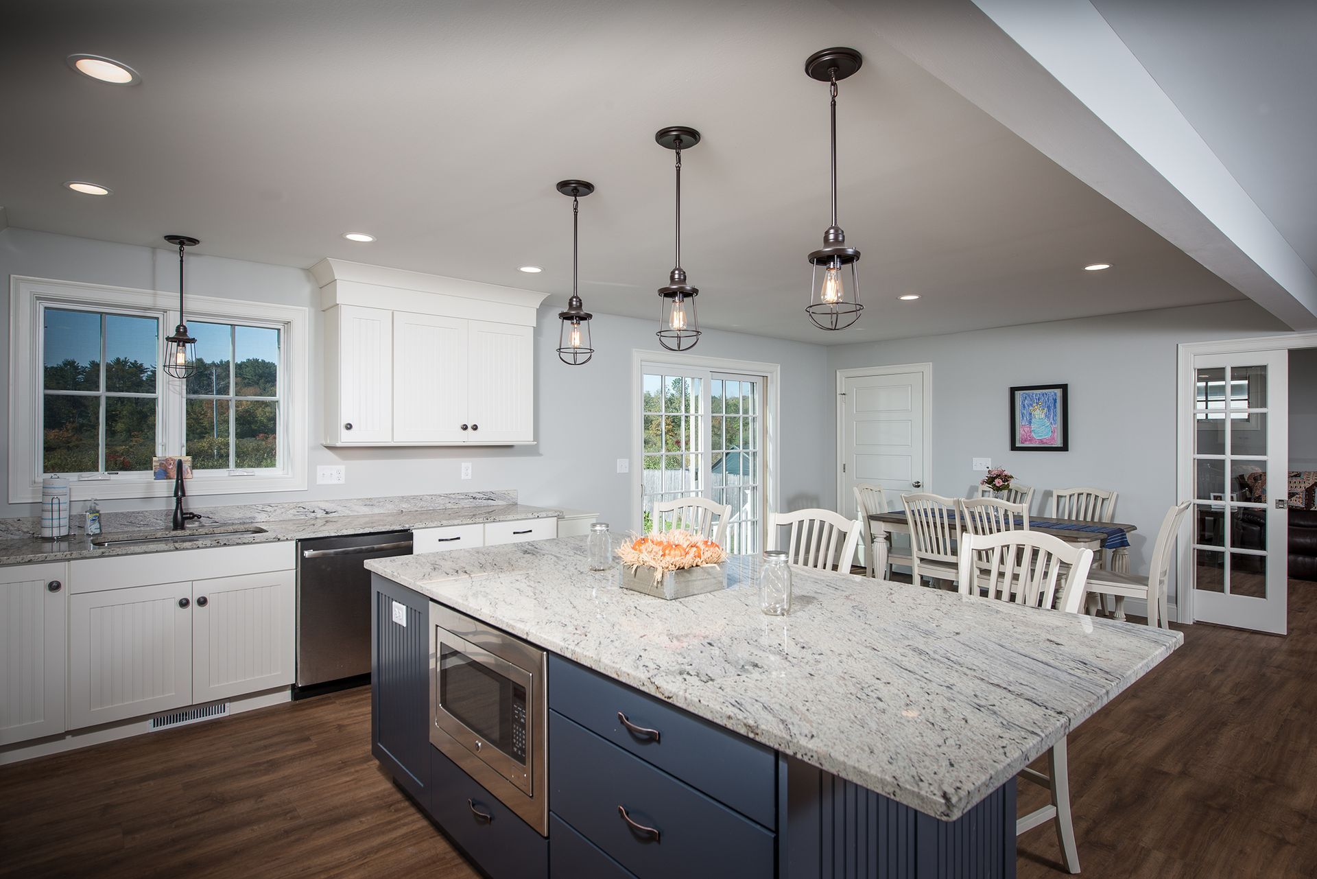 Modern kitchen with large island, white cabinets, pendant lights, and dining area by windows