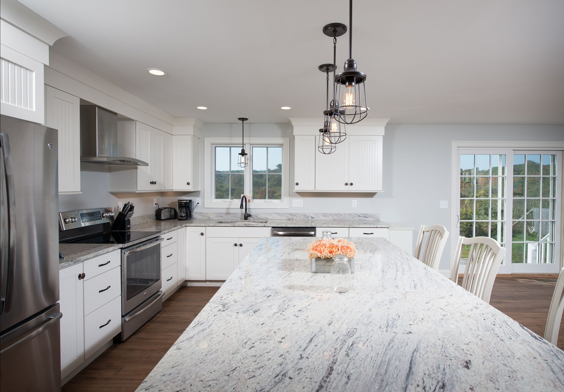 Bright white kitchen with a large marble island, stainless appliances, and hanging pendant lights.